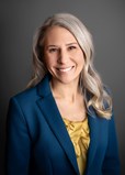 headshot of a smiling woman with light hair dressed in a grey suit